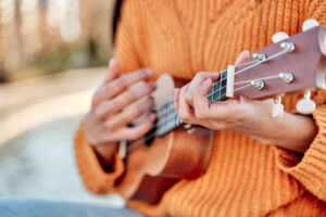 Close-up of girl playing ukulele in a garden with acoustic guitar, selective focus of woman hands playing ukulele strings.